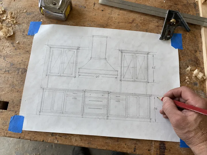 A cabinet maker’s pencil drawing of a kitchen wall, taped to his workbench.
